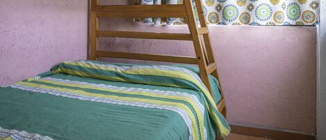 Una cama litera con una escalera de madera, una colcha a rayas verdes y blancas, y una cortina estampada.