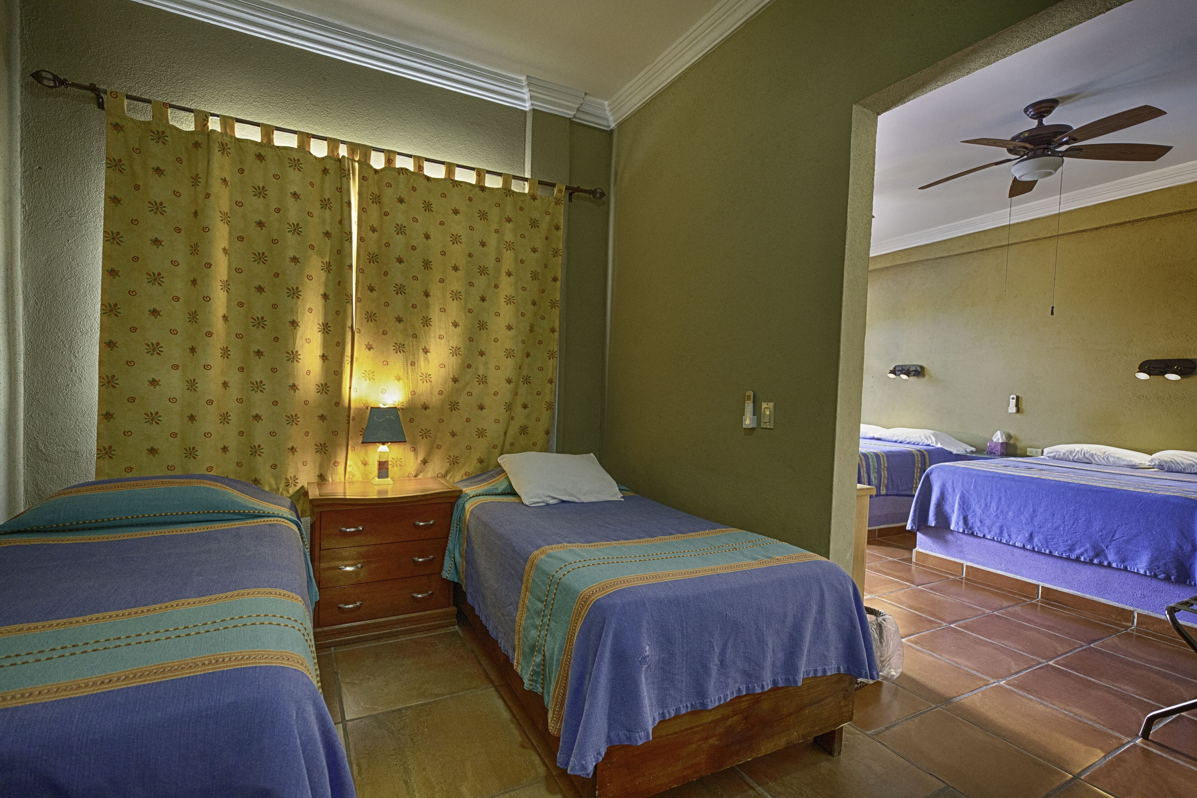 A room with two beds, a ceiling fan, and a window with curtains.