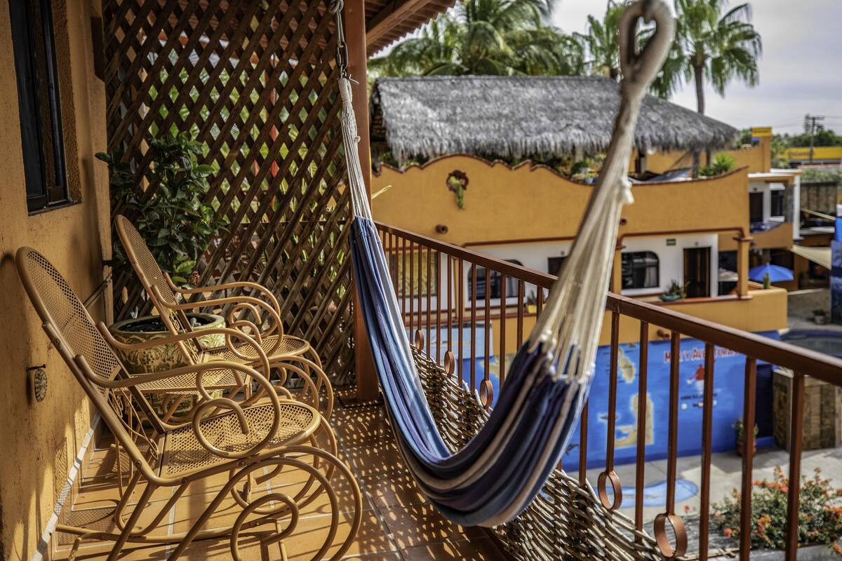 A balcony with wicker chairs, a hammock, and a view of a pool and buildings.