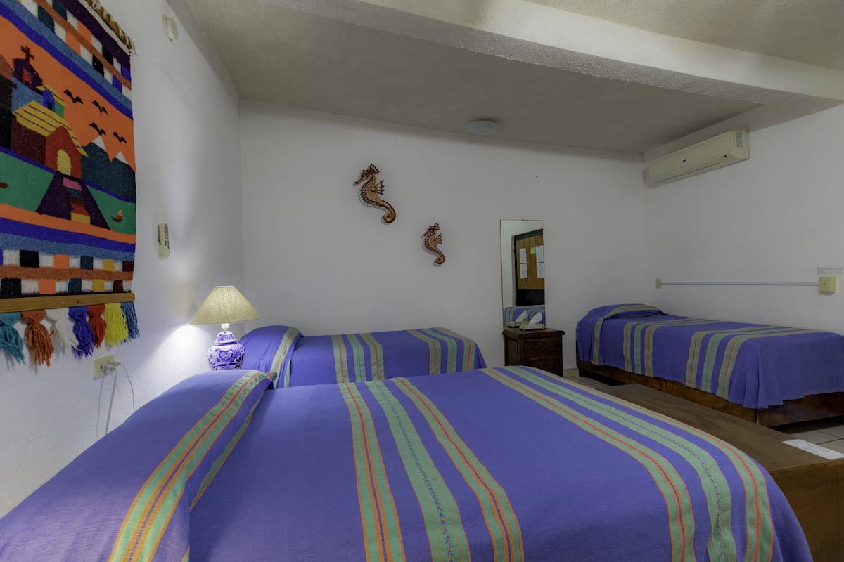 A hotel room with two beds, a colorful wall hanging, a lamp, and a mirror.