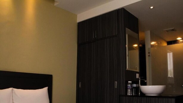 A hotel room with a bed, dark wooden wardrobe, and a bathroom with a white sink and mirror. - Zotel Hotel (Kuching)