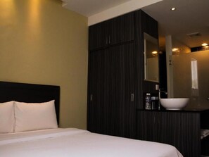 A hotel room with a bed, dark wooden wardrobe, and a bathroom with a white sink and mirror. - Zotel Hotel (Kuching)