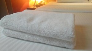 A neatly folded white towel on a bed with a striped pattern. - Zotel Hotel (Kuching)