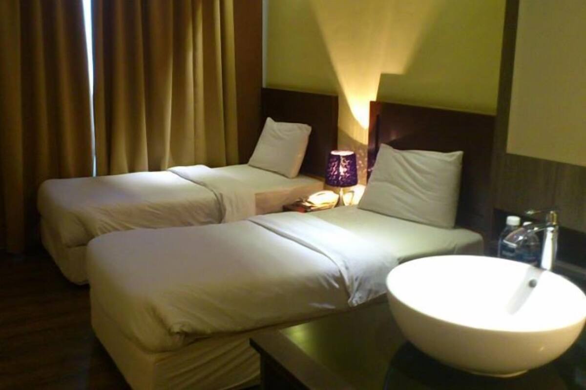 A hotel room with two beds, a bedside lamp, a round sink, and a window with curtains.