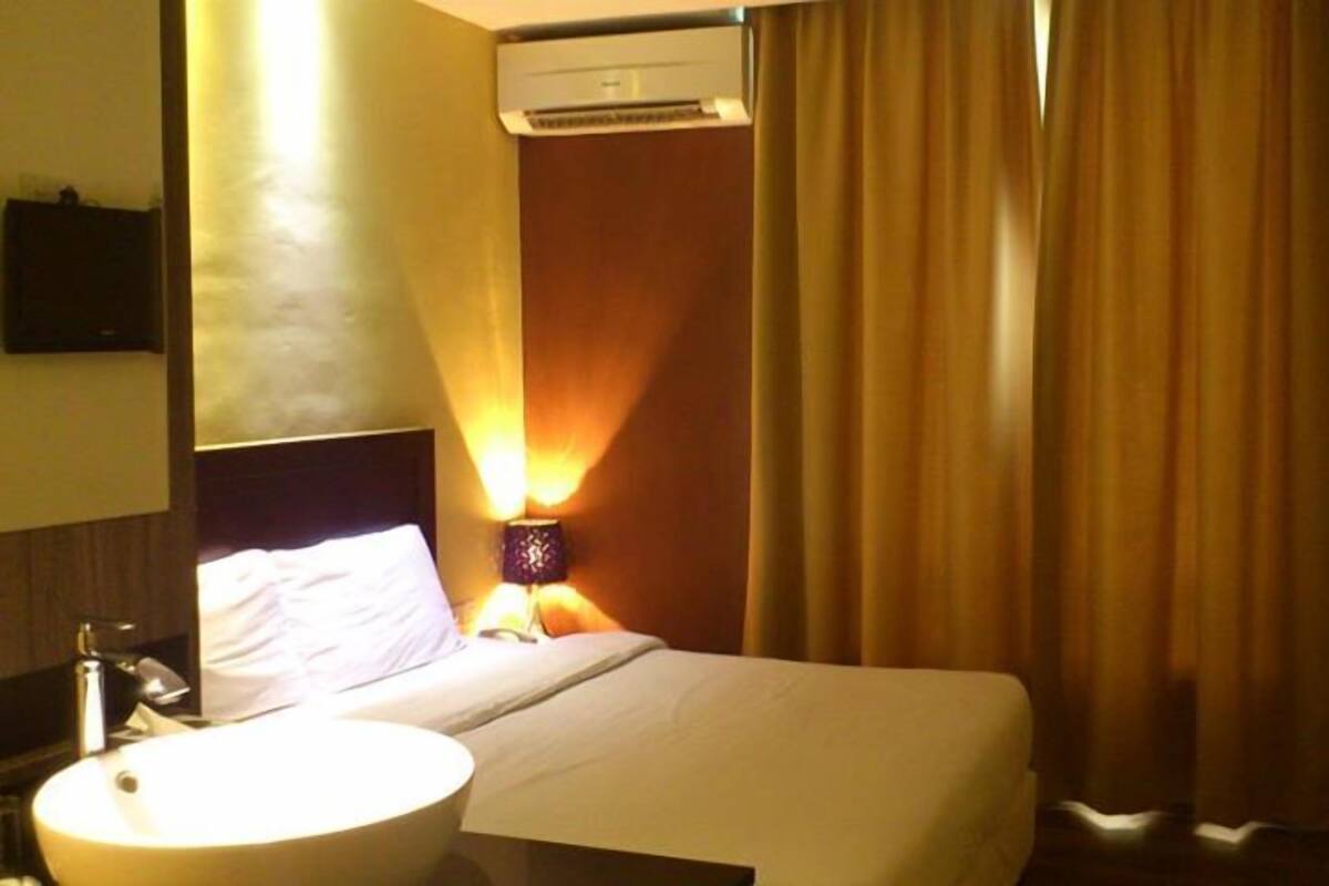 A hotel room with a bed, a round sink, a nightstand, an air conditioning unit, and a curtain.