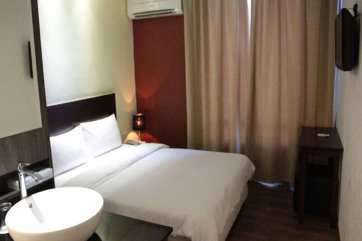 A hotel room with a bed, a round sink, a mirror, an air conditioning unit, a bedside table, and a television.