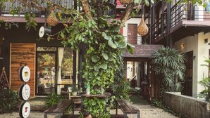 Un enfant est assis sur un banc en bois dans une cour, avec un café en arrière-plan.