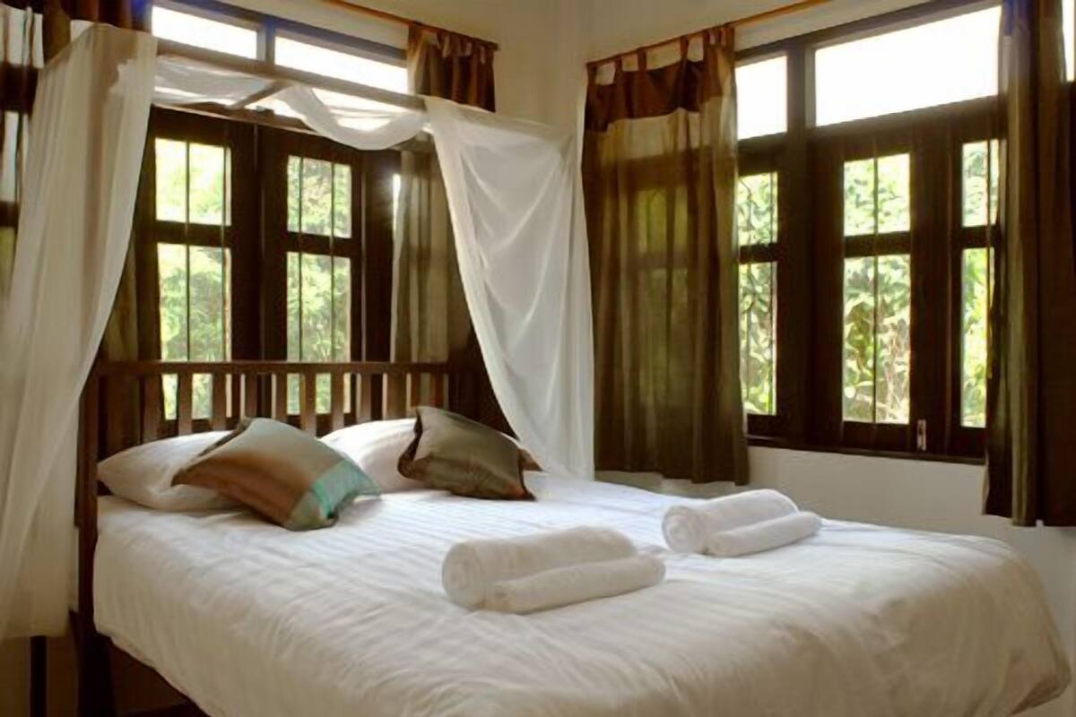 A bed with white linens, a canopy, and two towels.