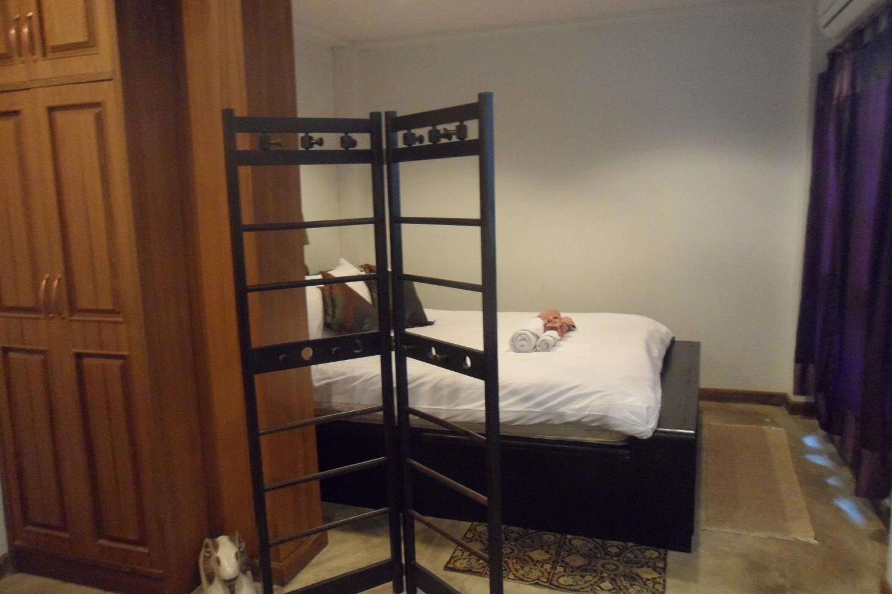 Una cama litera con escalera de madera, una mesita de noche y una cama con ropa de cama blanca.