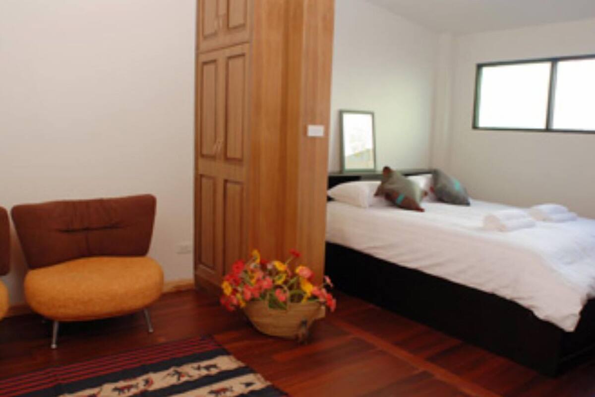 A bedroom with a bed, a chair, a wooden wardrobe, and a window.