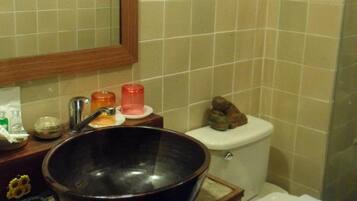 A bathroom with a large black basin, a wooden-framed mirror, a toilet, and a framed picture on the wall.