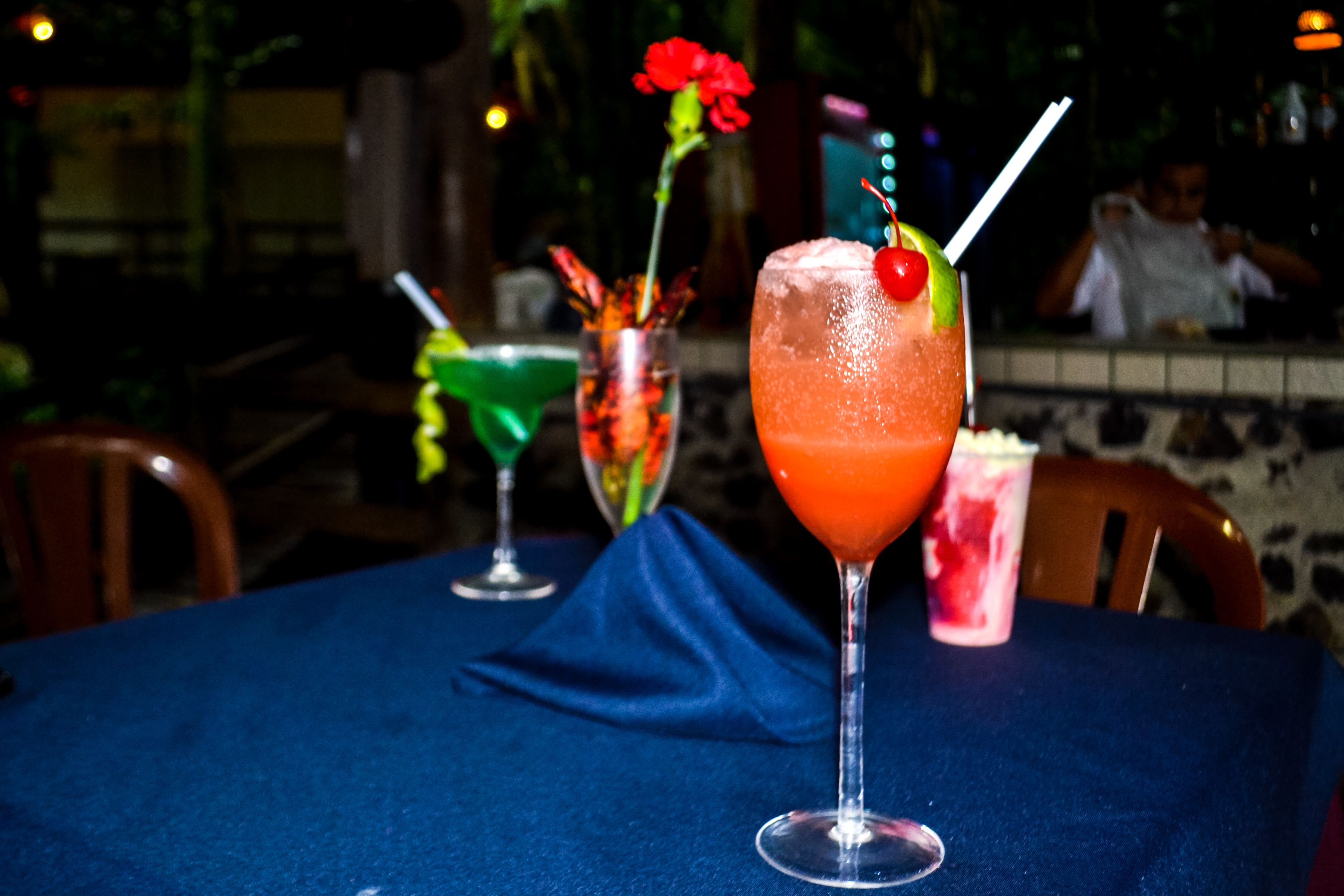 A table with a blue tablecloth, three drinks in martini glasses, and a person in the background.