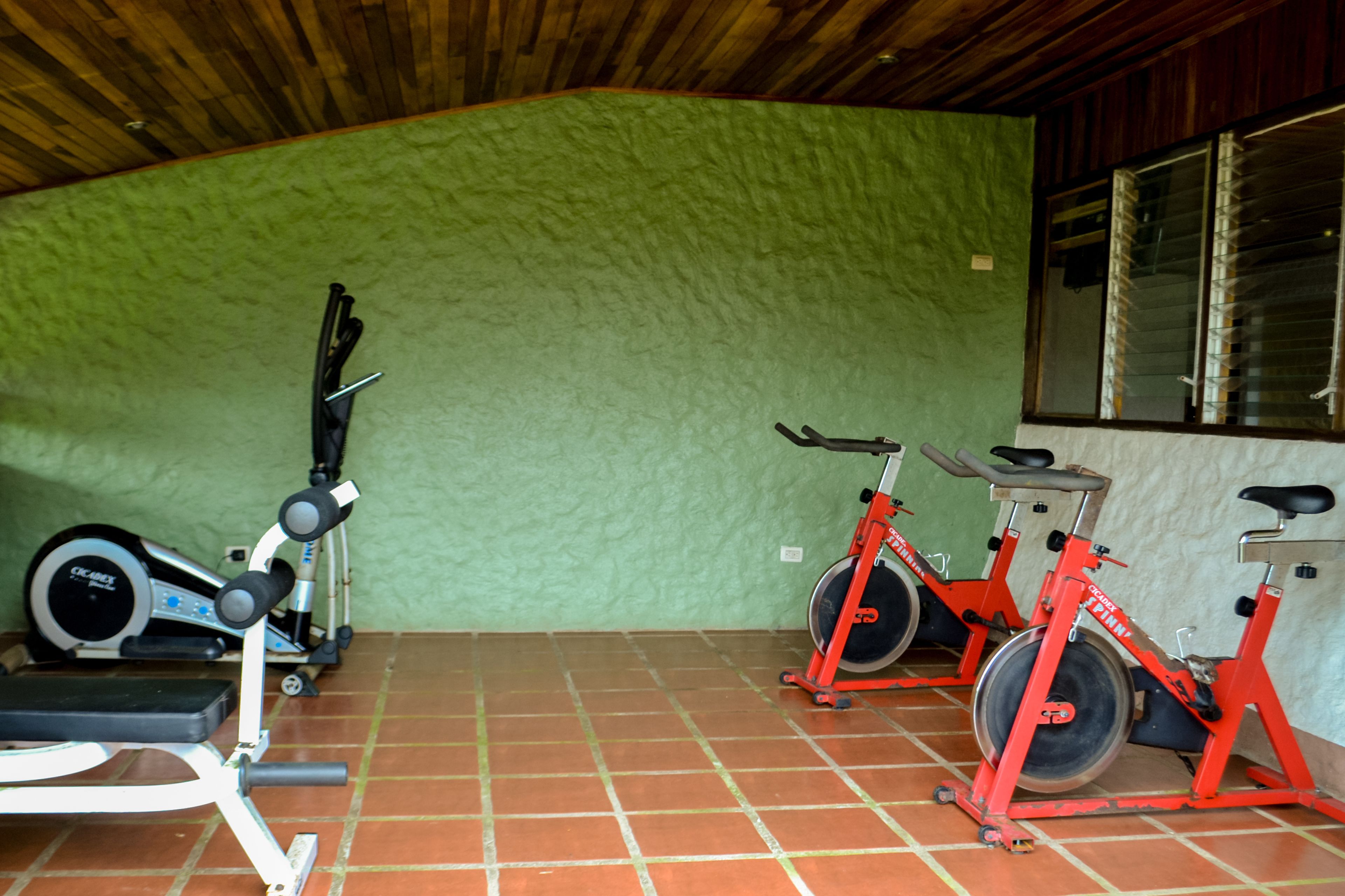 A gym with exercise equipment including a treadmill, stationary bikes, and a bench.