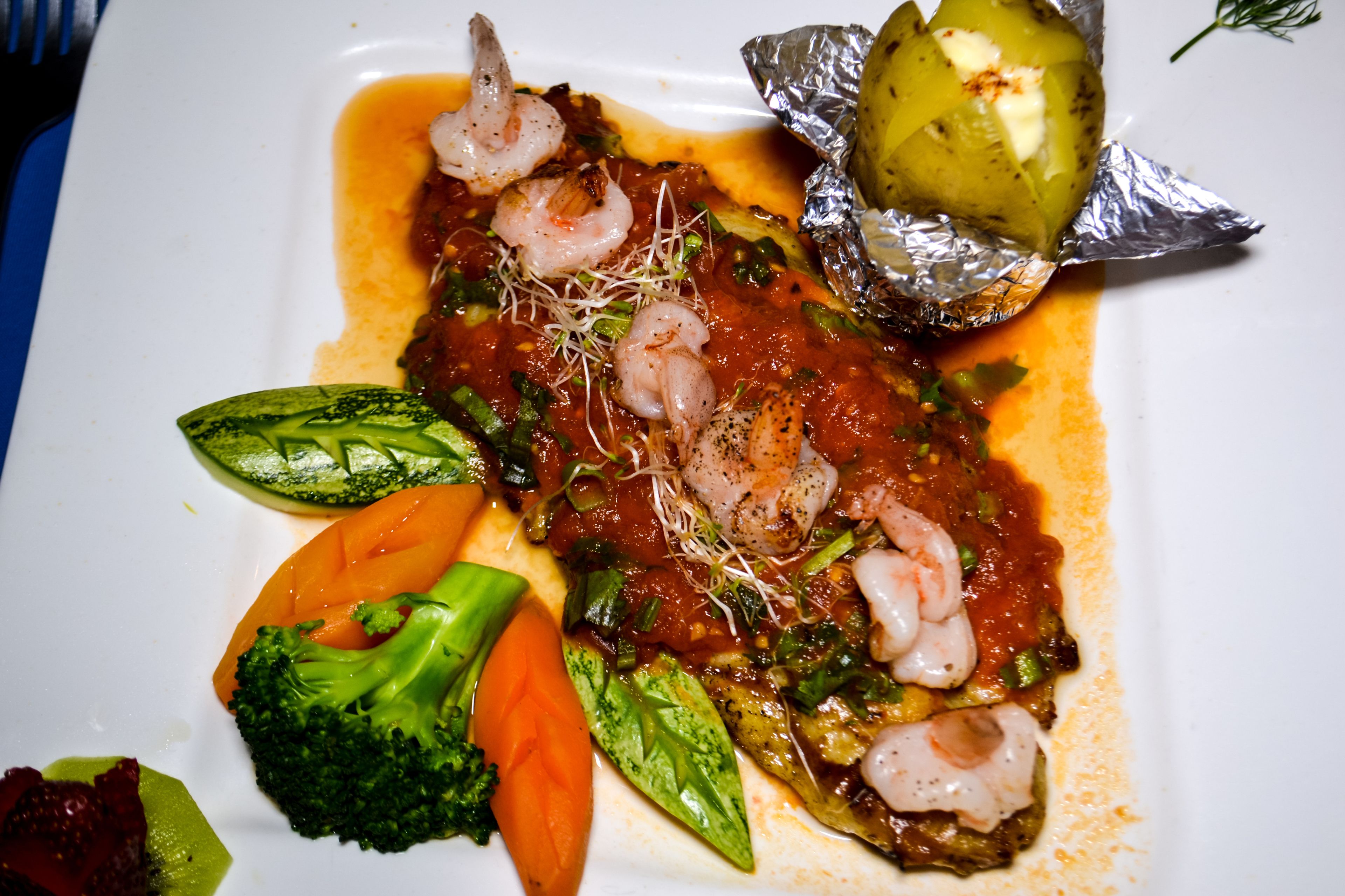 A plate of food with shrimp, vegetables, and a sauce.