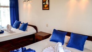 Habitación de hotel con dos camas, almohadas azules, un cuadro en la pared y una ventana con cortinas azules.