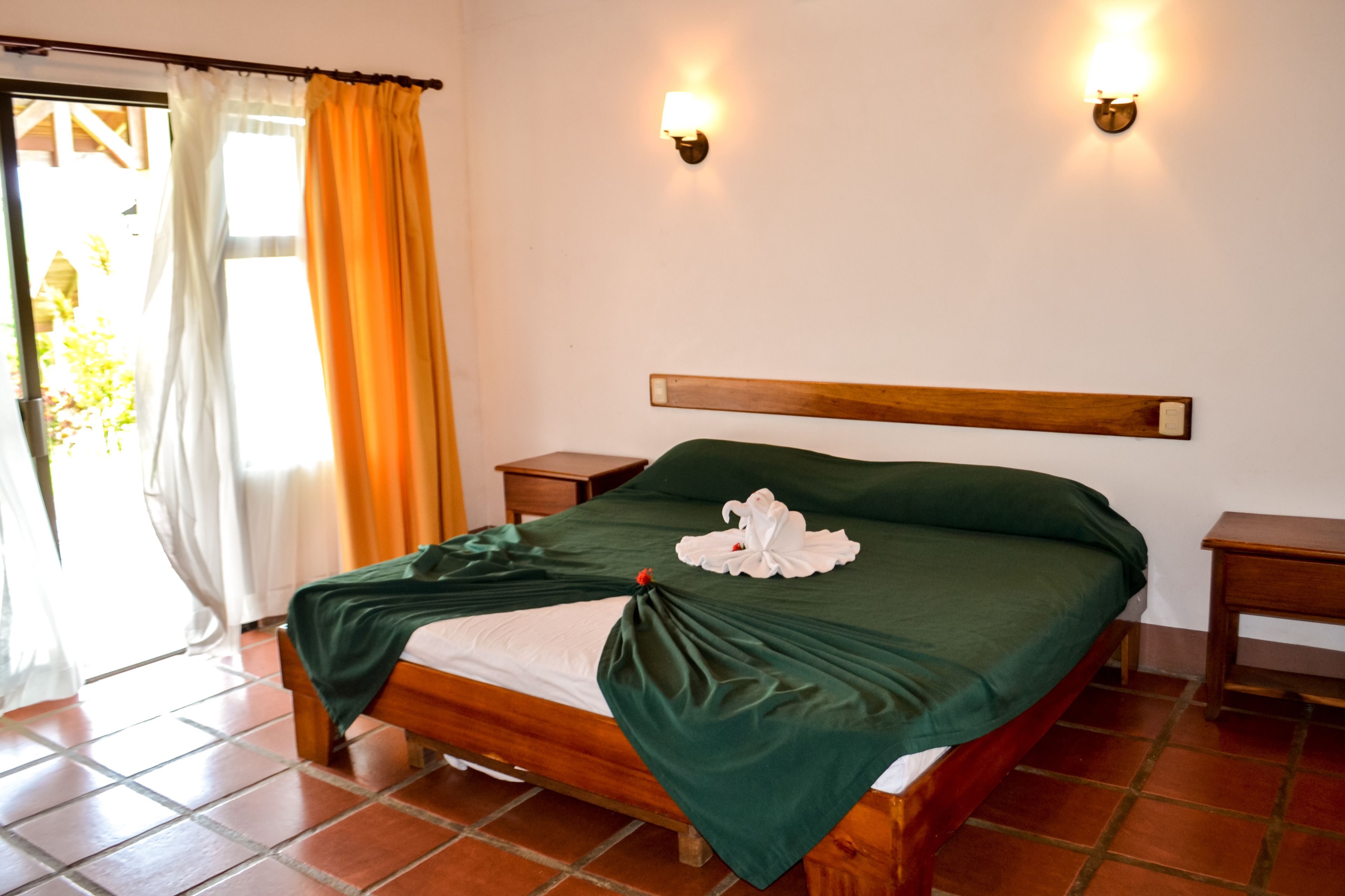 A neatly made bed with a green bedspread, two bedside tables, and two wall-mounted lights.