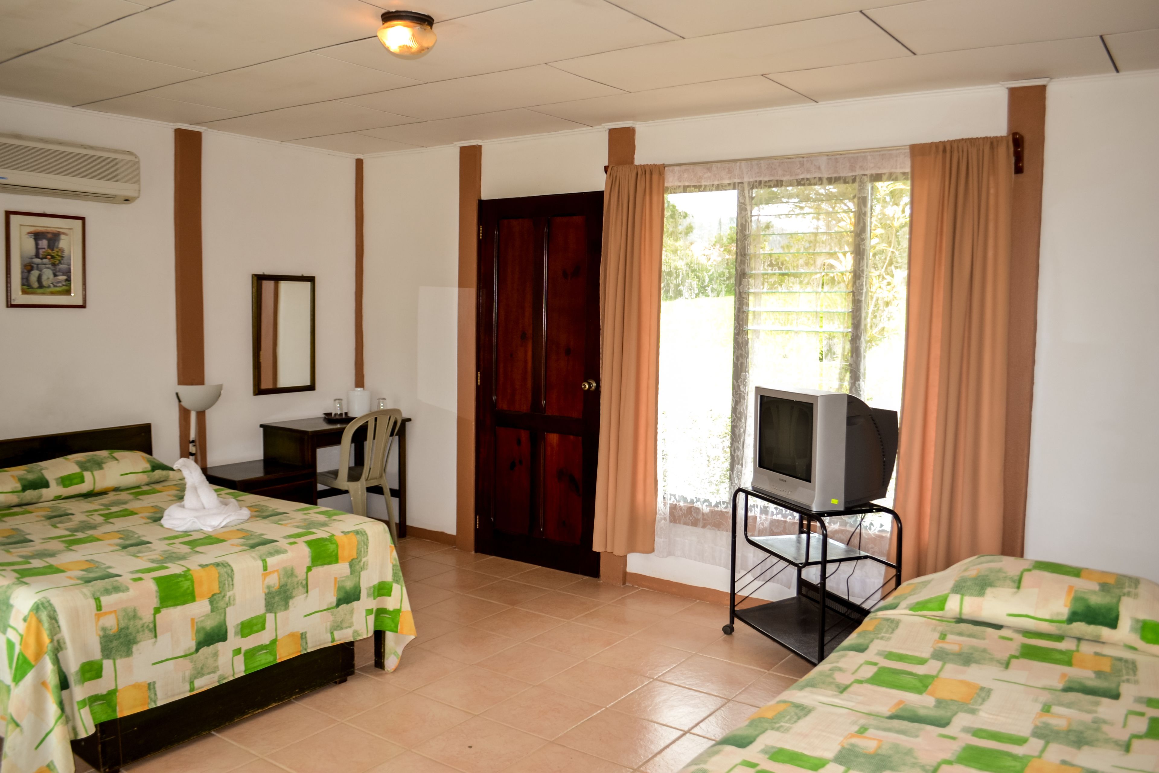 A hotel room with two beds, a television on a stand, a desk with a chair, and a door leading outside.