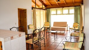 Una habitación amplia con suelo de baldosas, techo de madera, sofá, varias sillas y una mesa.