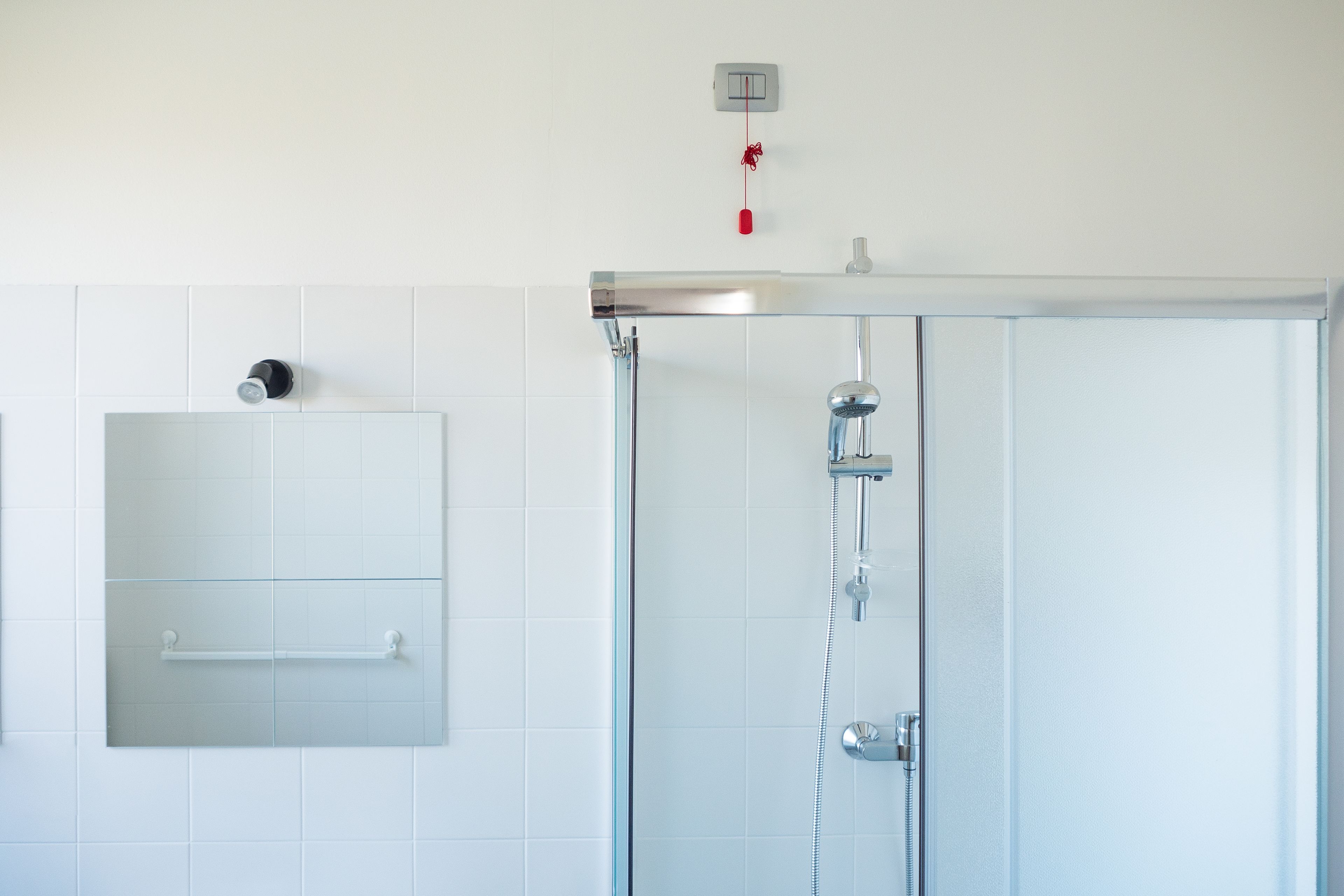 A bathroom with a glass shower enclosure, a towel rack, and a wall-mounted light switch.