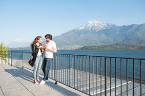 A couple standing on a waterfront promenade with a mountain backdrop. - Lake Como Beach Hostel (Domaso)