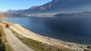 A lake with a mountain in the background and a road leading to a building. - Lake Como Beach Hostel (Domaso)