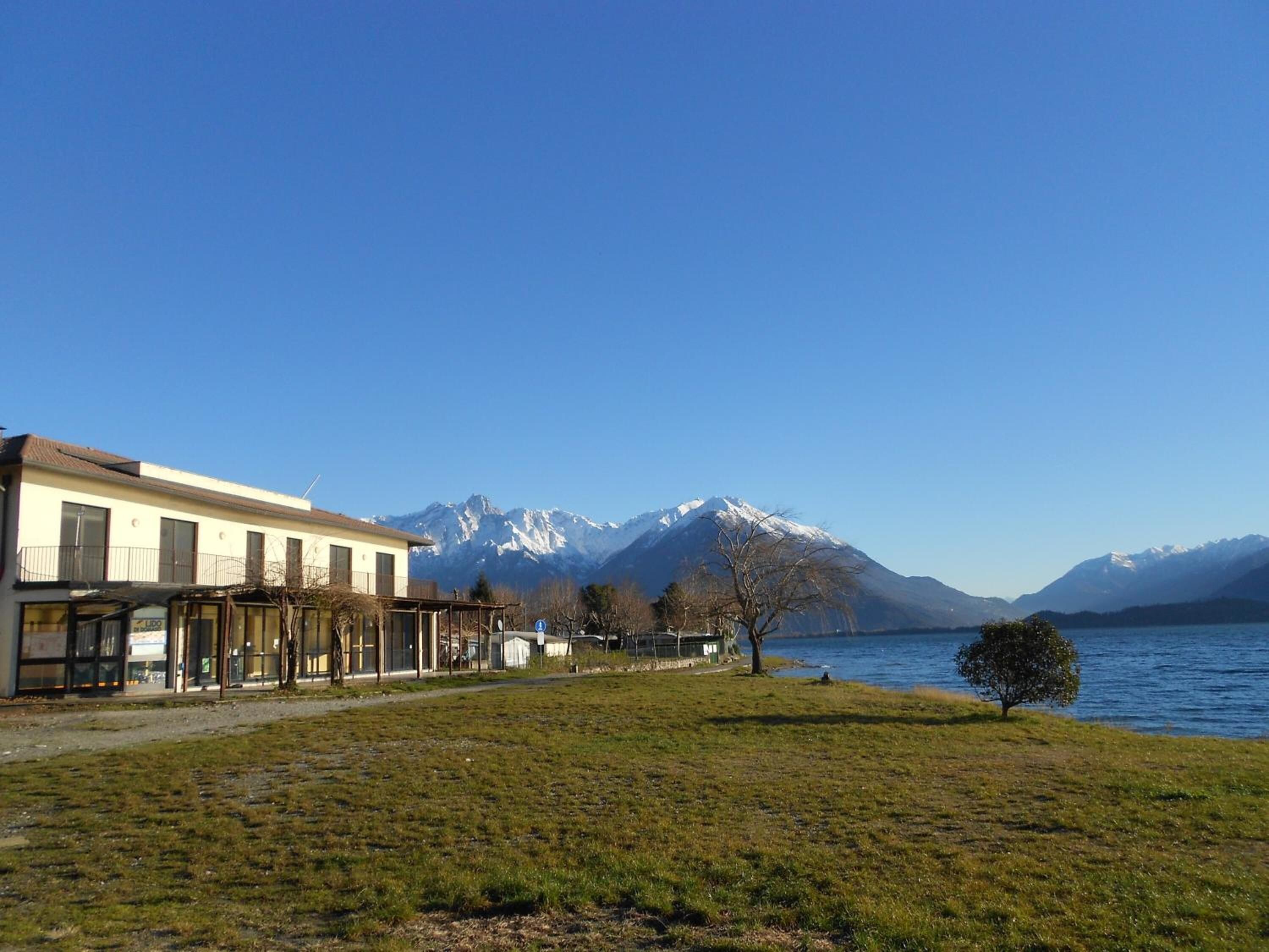 Un bâtiment doté d’une façade en verre, d’une zone verdoyante et d’un lac, avec des montagnes en arrière-plan.