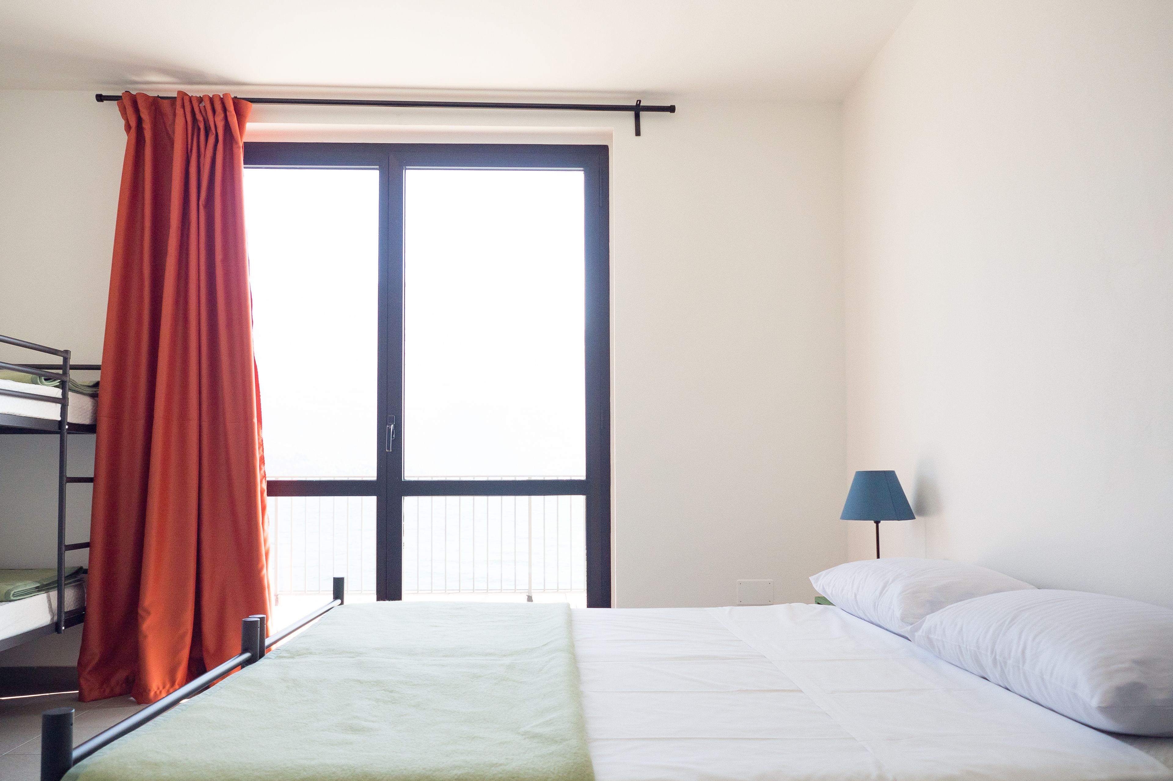Una cama individual con una colcha verde, un almohadón blanco y una cortina naranja.