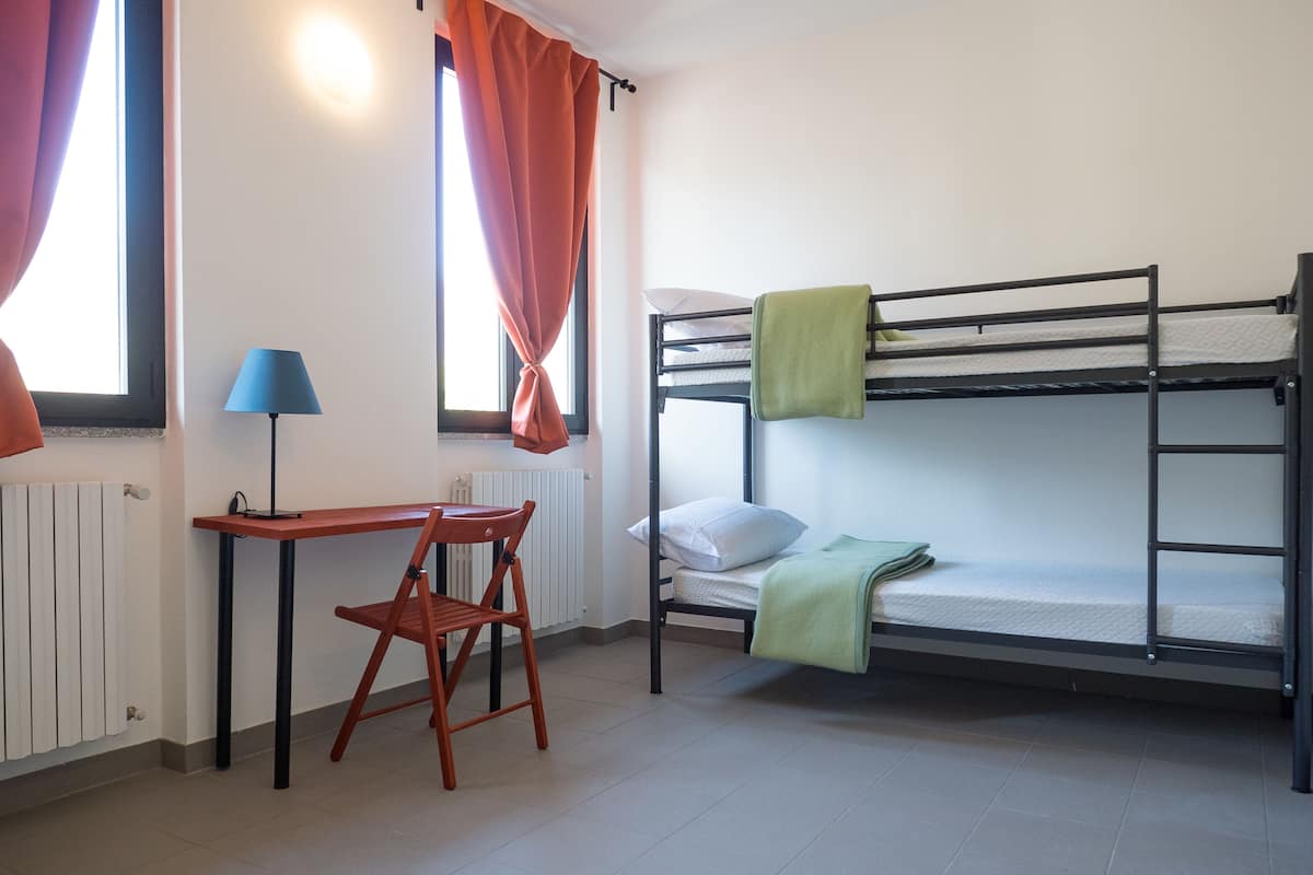 A bunk bed with a desk and chair, a lamp, and a window with curtains.