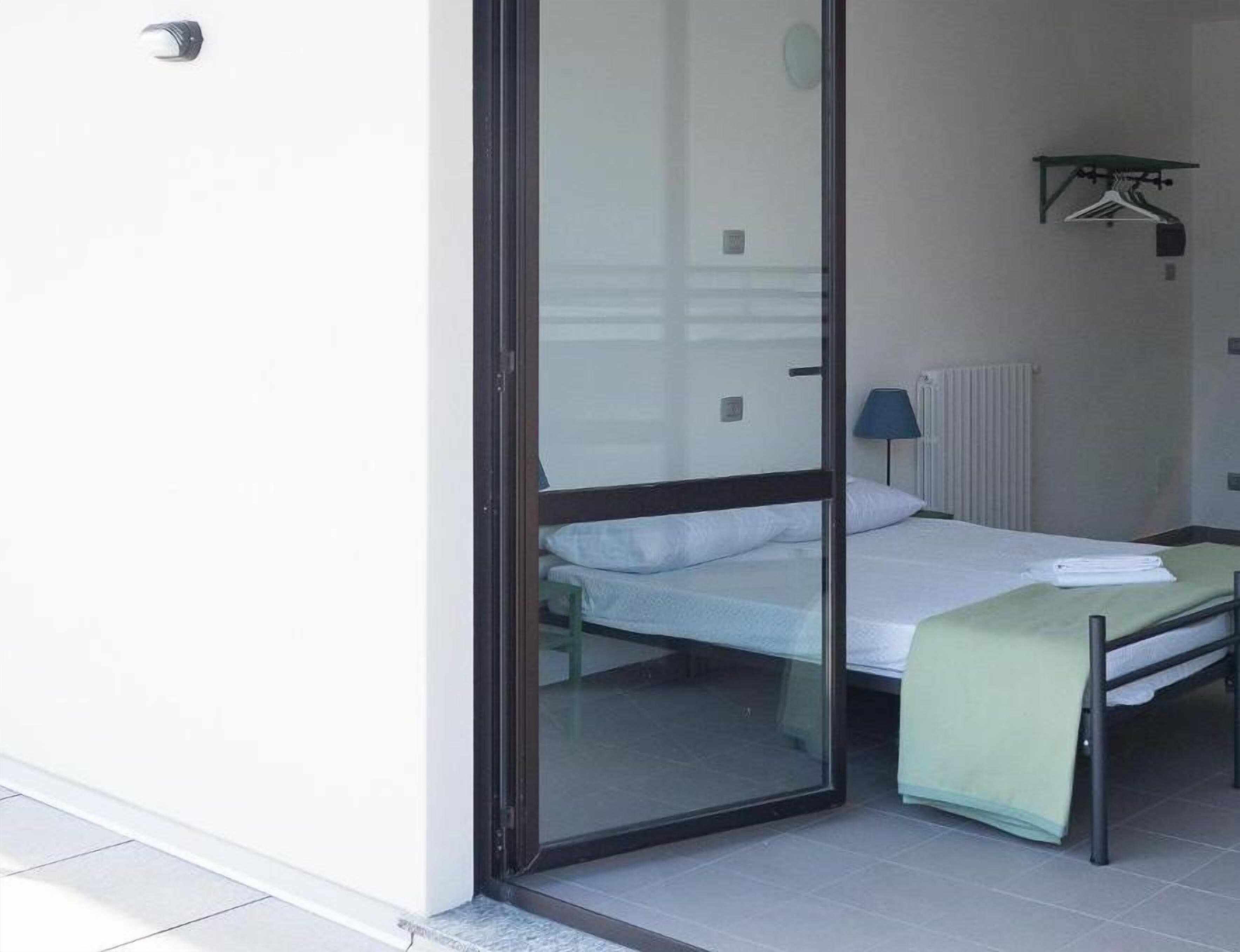 Quarto individual com uma porta de correr para varanda, radiador e cabideiro fixado na parede.