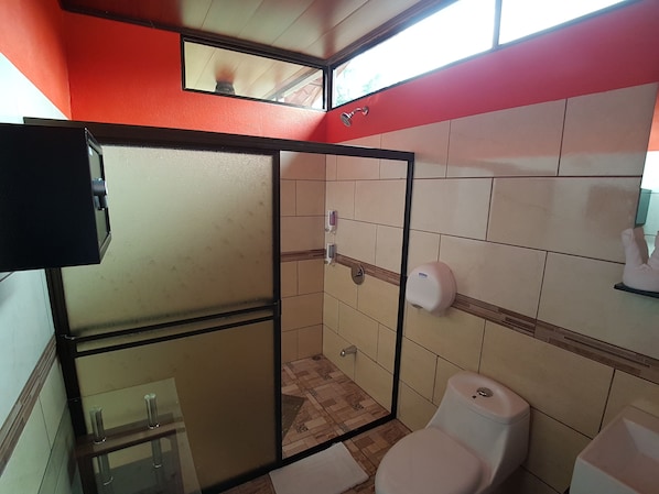 Un baño con cabina de ducha de vidrio, inodoro y secamanos.