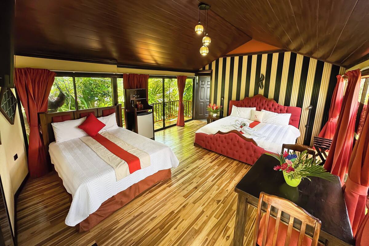 Ein Zimmer mit zwei Betten, einem kleinen Tisch mit einer Vase und Blick auf Grünfläche.