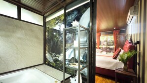 A modern bathroom with a large bathtub, a glass shower enclosure, and a view of a waterfall through the glass. - Hotel Heliconias Nature Inn & Hot Springs (Peñas Blancas)