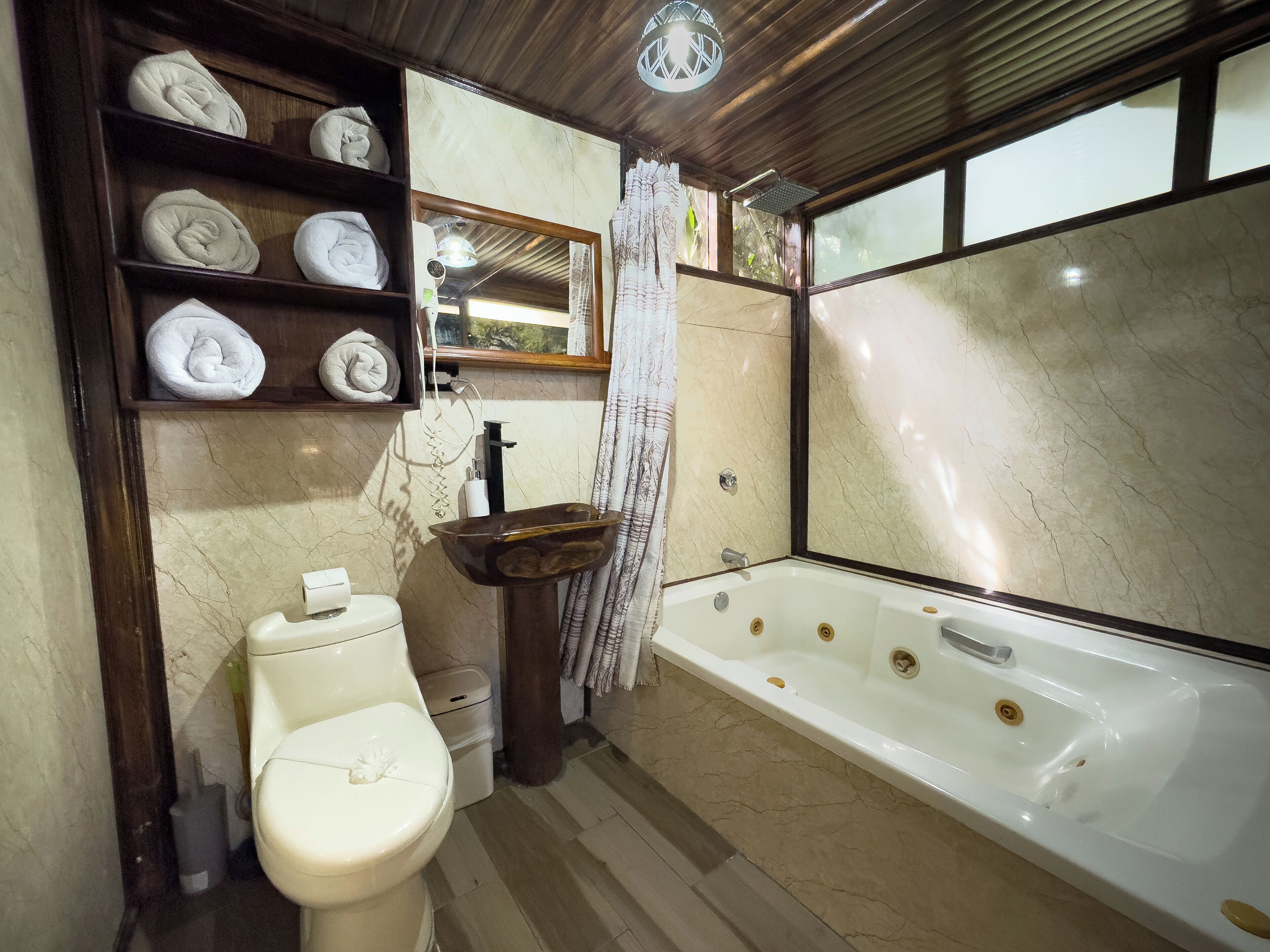 A bathroom with a toilet, sink, and bathtub. There are shelves with towels and a shower curtain.