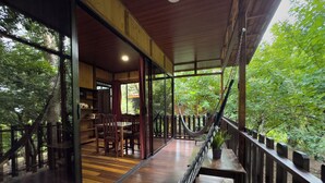 A wooden deck with a hammock, a dining area with chairs, and a view of lush greenery. - Hotel Heliconias Nature Inn & Hot Springs (Peñas Blancas)
