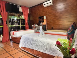 Habitación de hotel con dos camas, un ventanal grande con cortinas, una pared de madera y una mesita con una toalla y una almohada.
