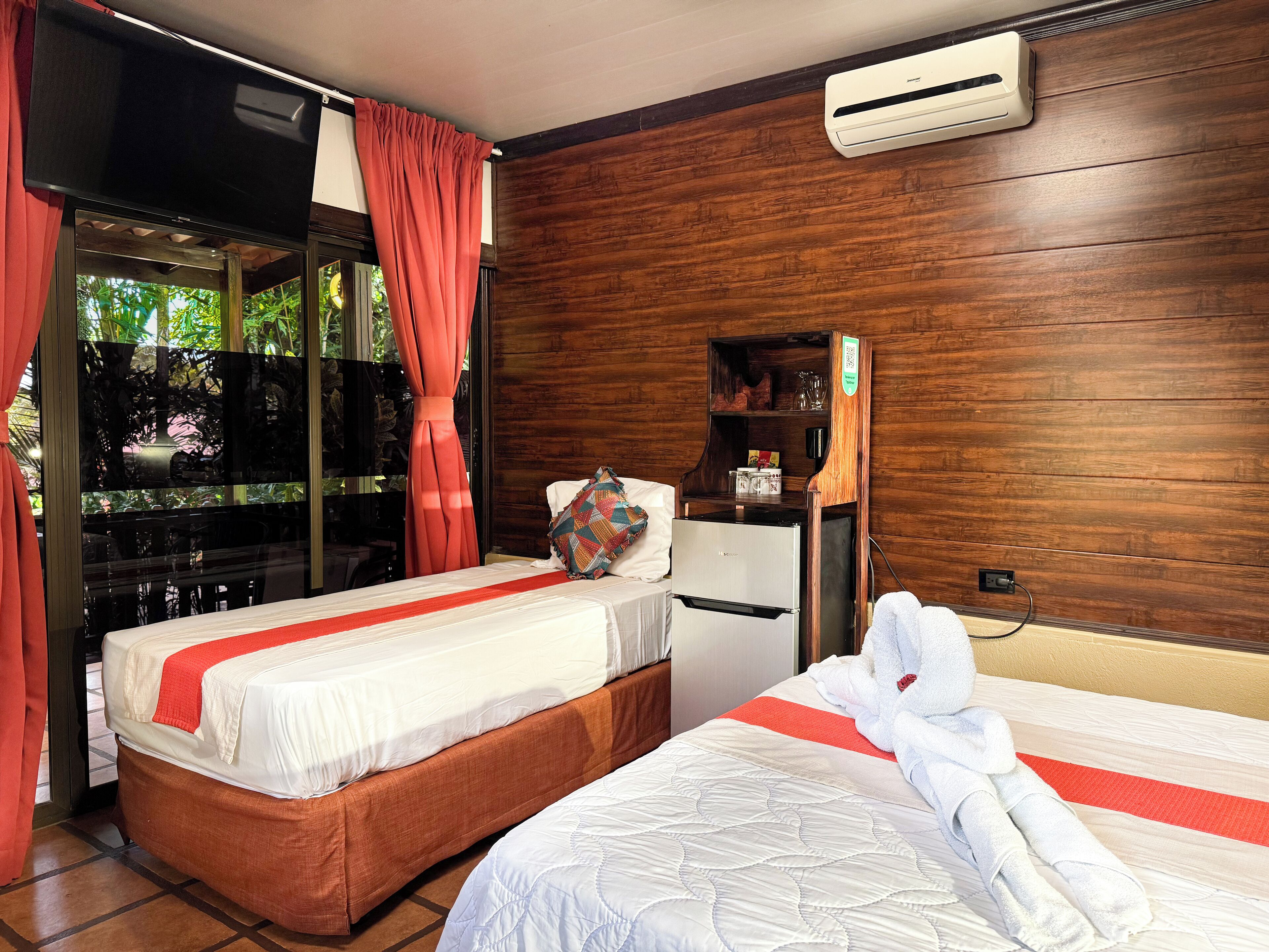 Habitación de hotel con dos camas, un minibar, un equipo de aire acondicionado y vista a través de un ventanal.