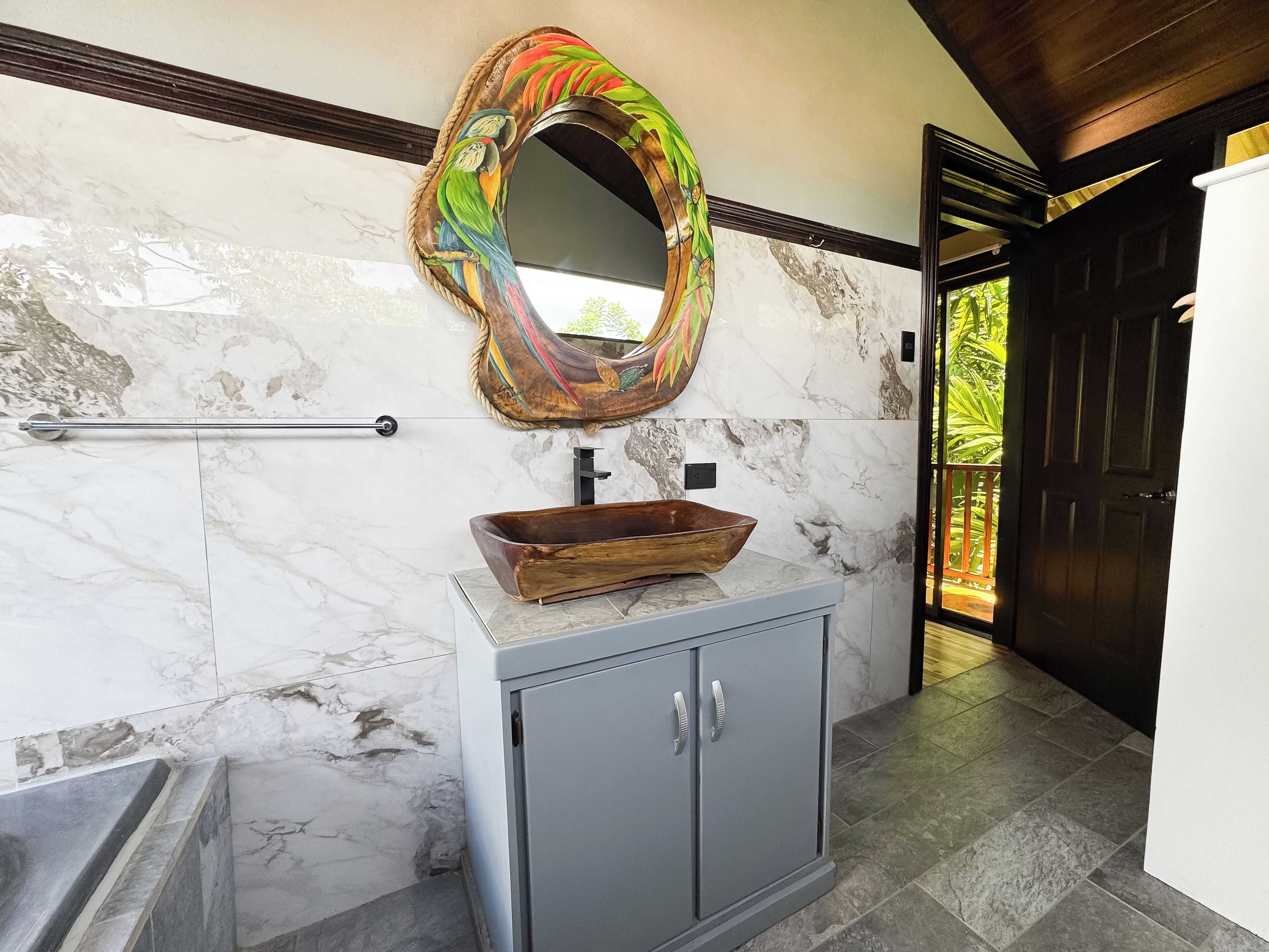 A bathroom with a marble wall, a wooden basin sink, and a colorful mirror.