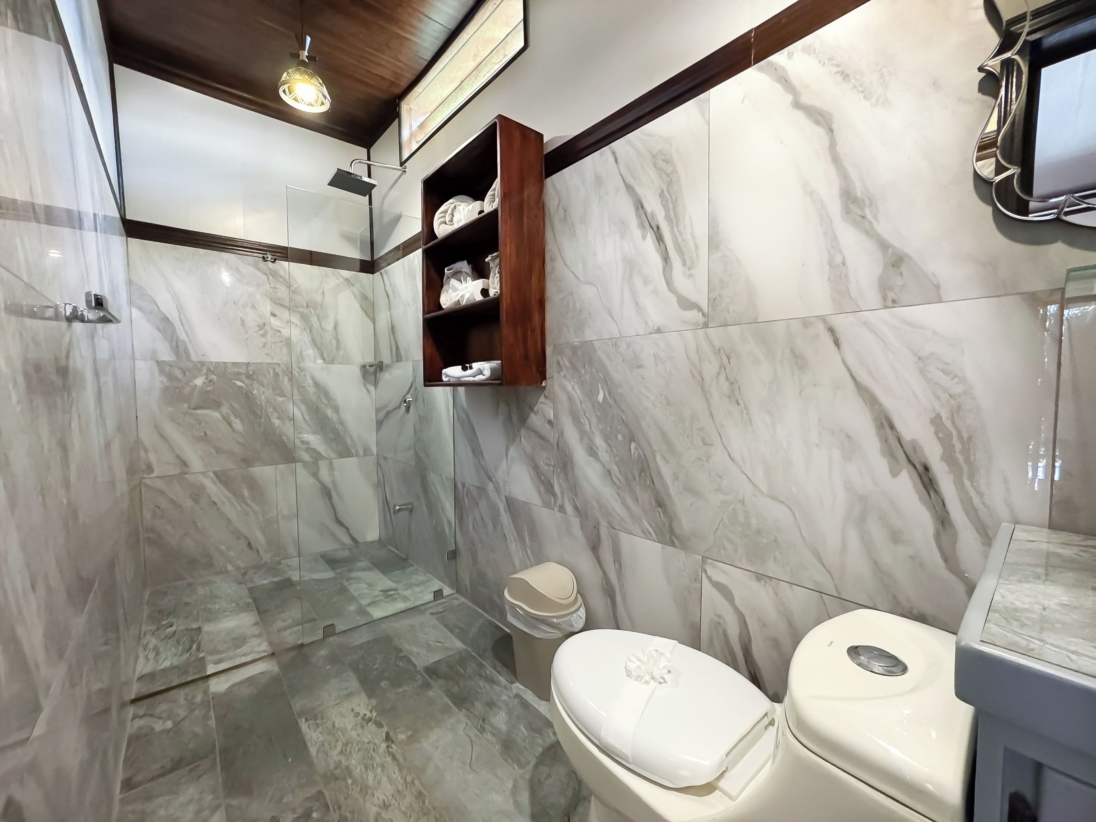 A bathroom with marble walls, a shower, a toilet, and a wooden shelf with toiletries.