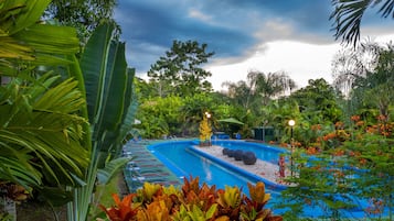 Ein Schwimmbecken, umgeben von tropischer Vegetation und einem bewölkten Himmel.