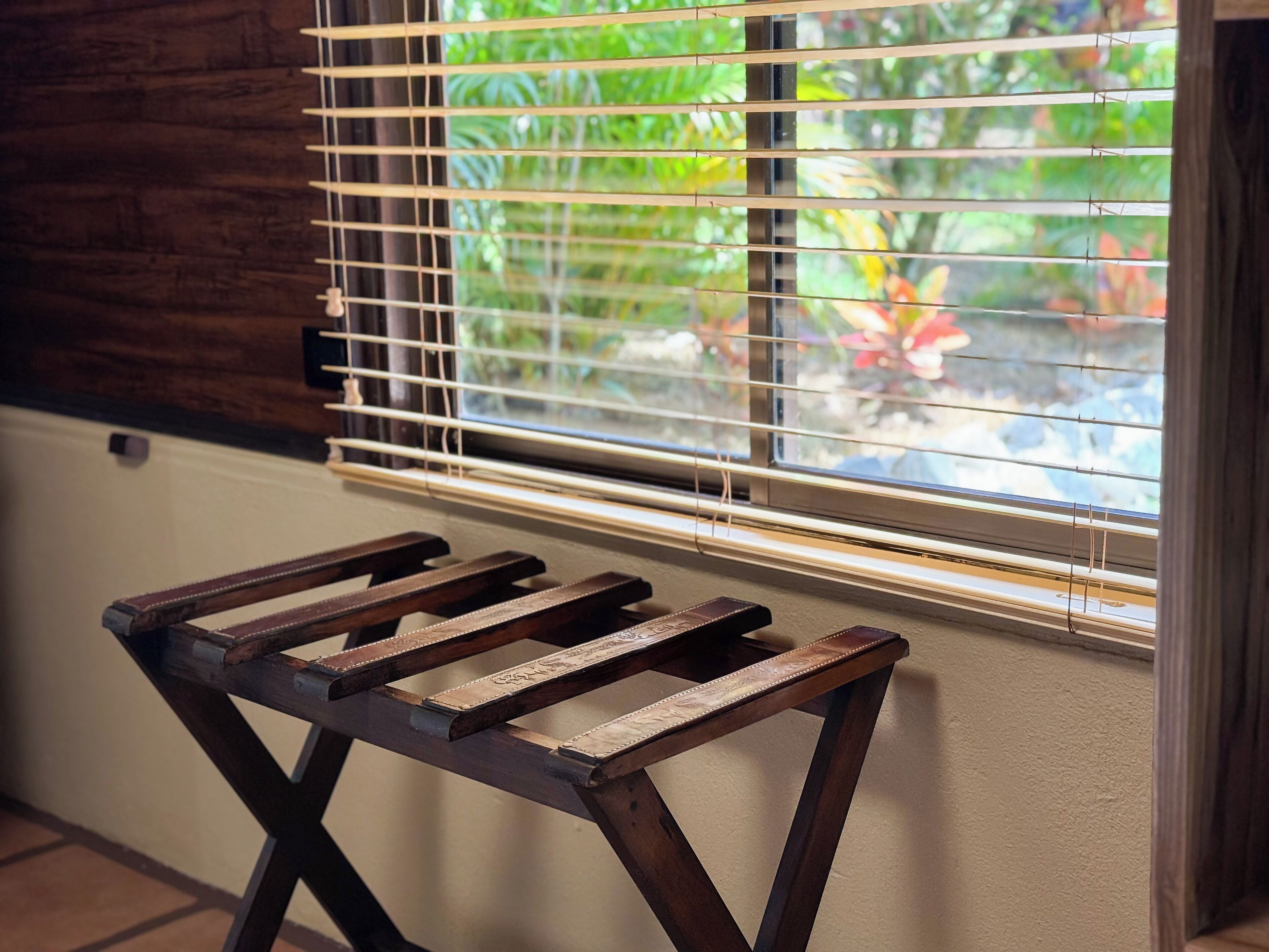 A wooden stool with a metal frame, positioned in front of a window with horizontal blinds.