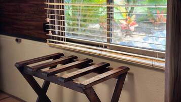 A wooden stool with a metal frame, positioned in front of a window with horizontal blinds.