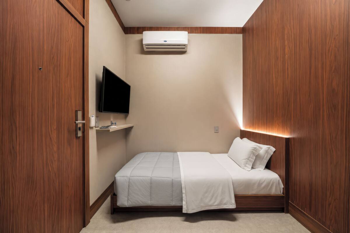 Ein Schlafzimmer mit einem Bett, einem Wand-Fernseher, einer Klimaanlage und einem Holzschrank.