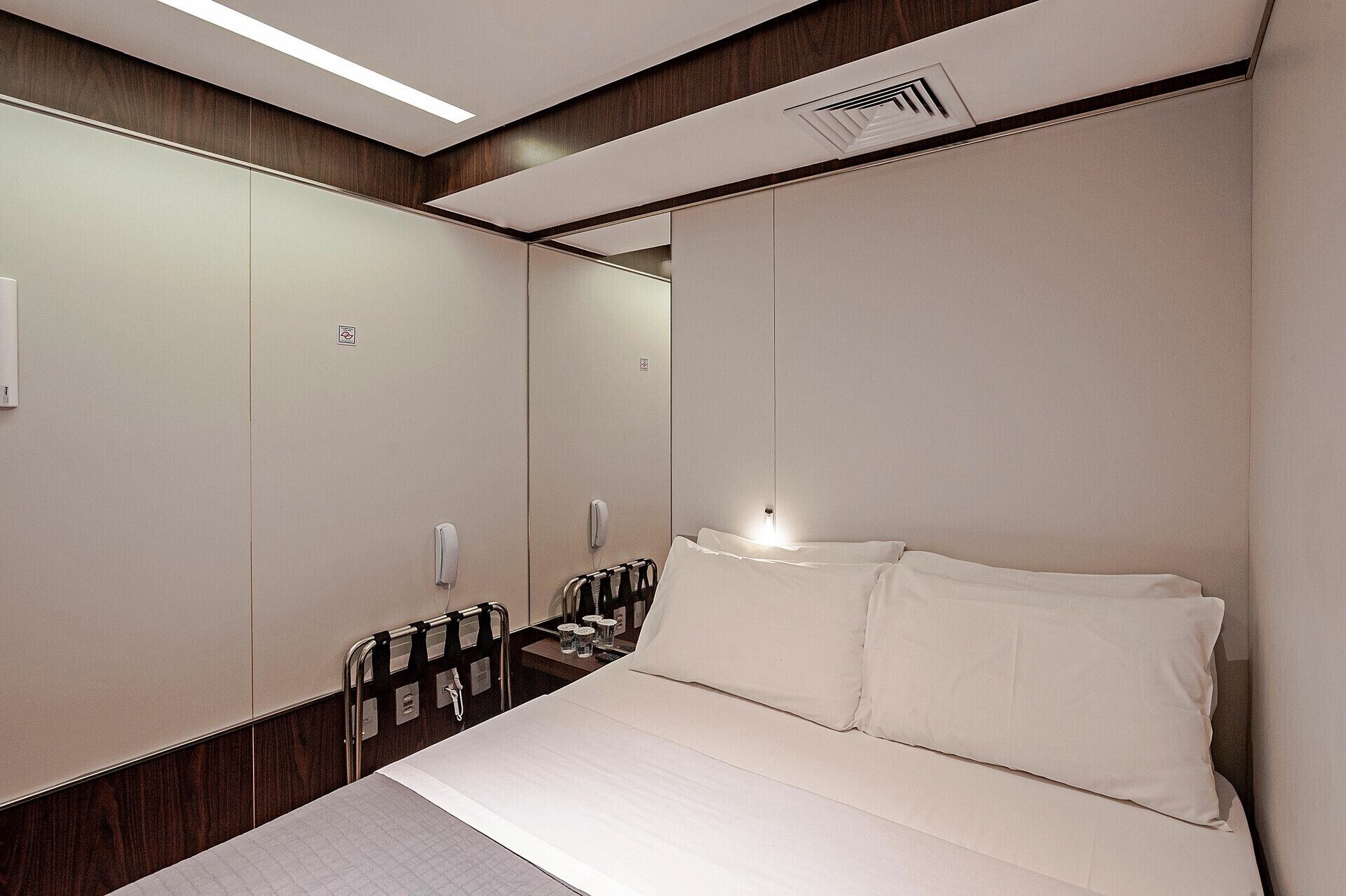 Quarto de hotel com uma cama grande, mesa de cabeceira, espelho e guarda-roupa.