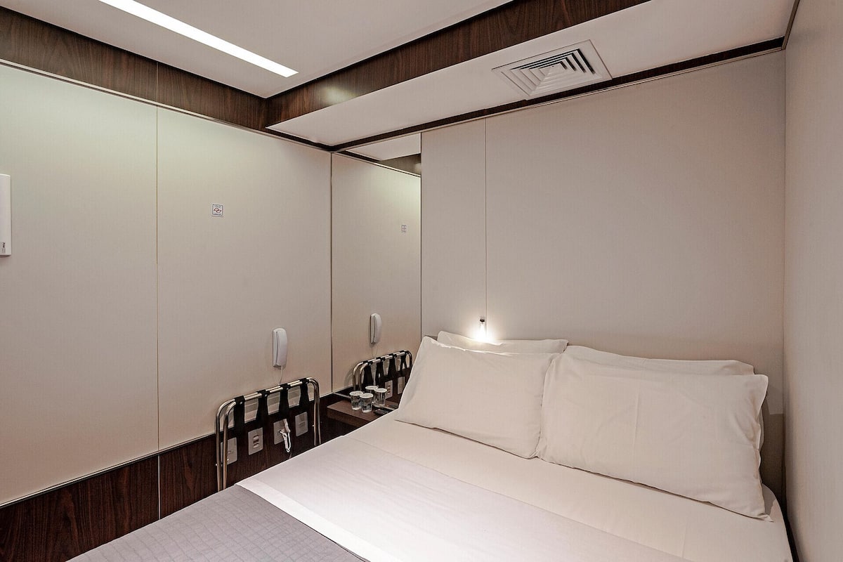 A hotel room with a large bed, a bedside table, a mirror, and a wardrobe.