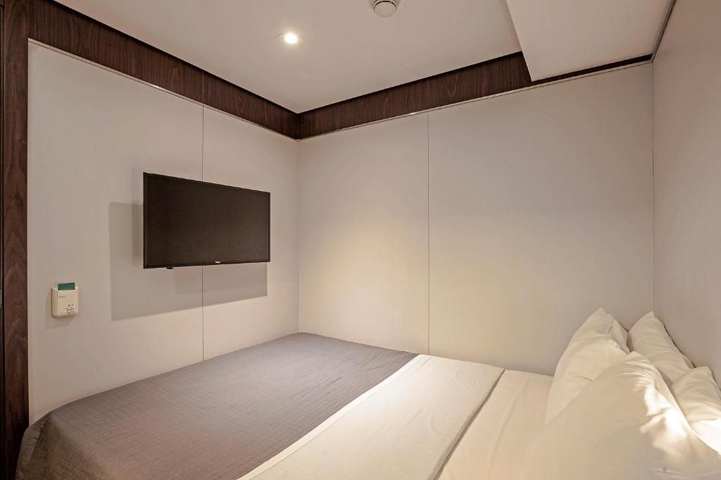 A bedroom with a bed, a flat-screen TV mounted on the wall, and a thermostat on the wall.