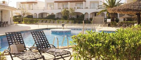 Area piscina con sedie a sdraio, vasca idromassaggio e vista sugli edifici dell'hotel.