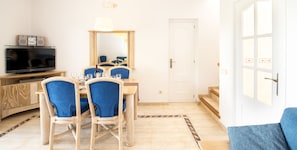 A dining area with wicker chairs, a wooden table, a television, and a mirror.