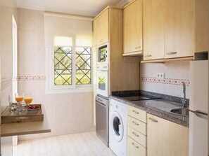 Une cuisine compacte avec des meubles en bois, un four encastré, un lave-linge et un plan de travail en granit.
