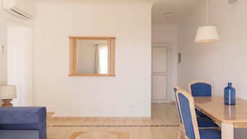 Uma sala de jantar com mesa de madeira, cadeiras estofadas em azul, um espelho na parede e um sofá azul.