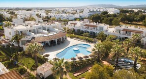 A resort with multiple white buildings, a central swimming pool, and palm trees. - Ona Village Cala d'Or (Santanyi)
